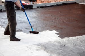 roofer applying roof coating on a concrete roof.
