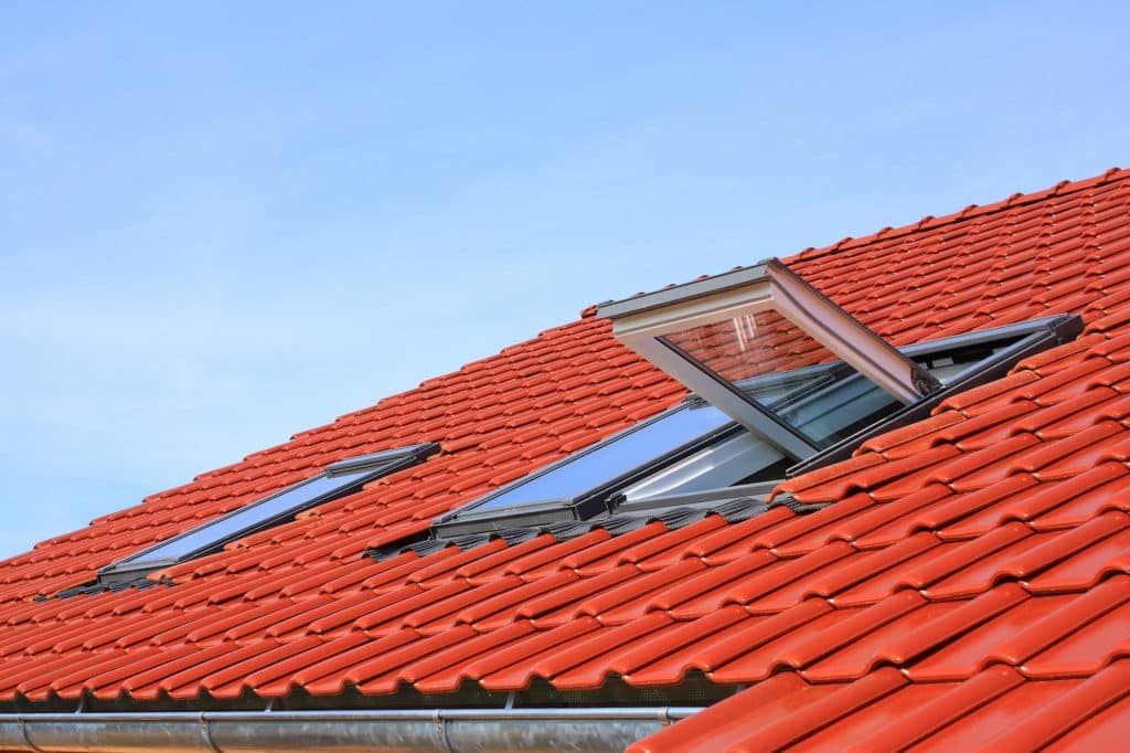 Red clay tile roof with two roof windows, one of them open, against a clear sky