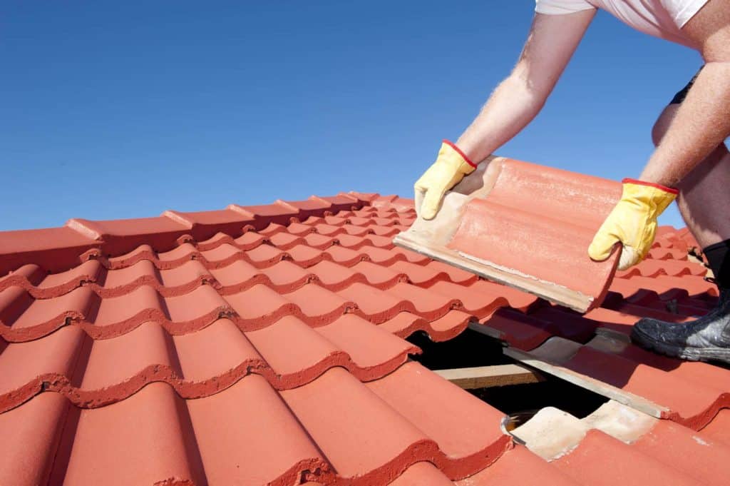 Gloved hands placing a red clay roof tile onto a partly tiled roof